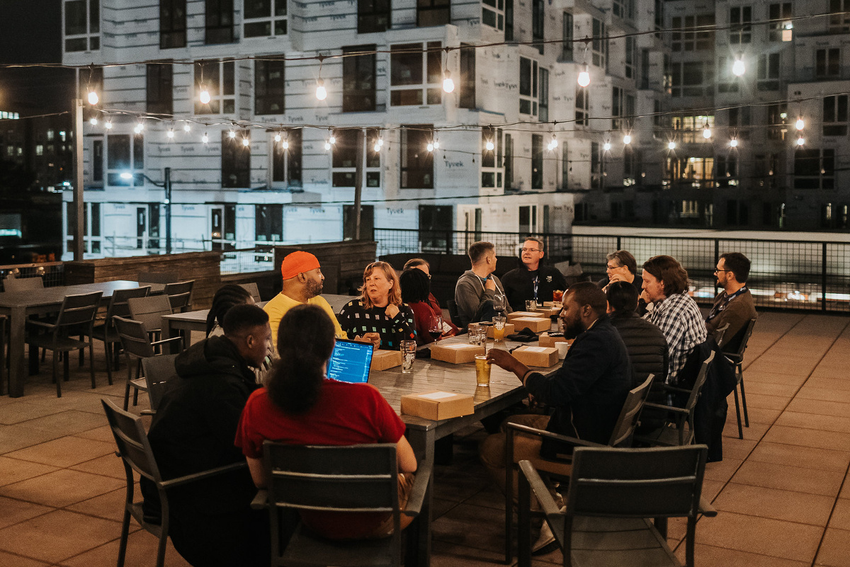 A group of speakers and organizers of DjangoCon US 2023 sitting around a table, outdoors at night in Durham, NC.